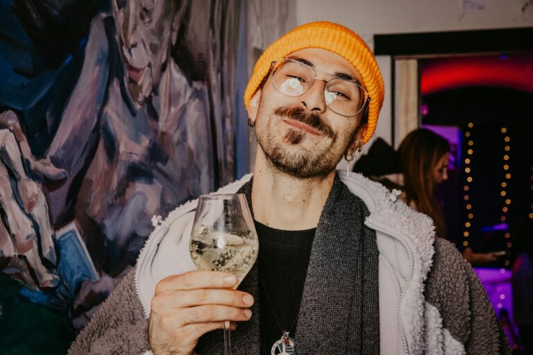 Smiling man enjoying wine at an art gallery party with vibrant ambiance.